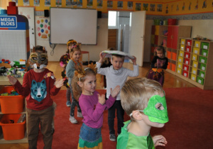 Dzieci w przebraniach i maskach patrzą na coś poza kadrem.